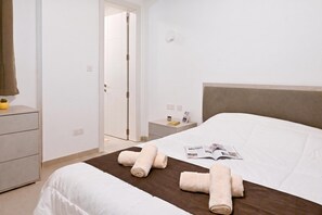 A hotel room with a bed, a nightstand, a dresser, and a door. - Pool And Sea - Modern Apart Sannat Gozo, Sannat Ghawdex - Gozo, Malta (Sannat Ghawdex - Gozo)