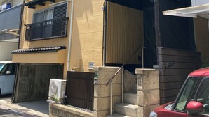 A multi-story residential building with balconies, a gated entrance, and a red car parked in front. - Neo Universal 01 (Osaka, Konohana, Nishikujo)