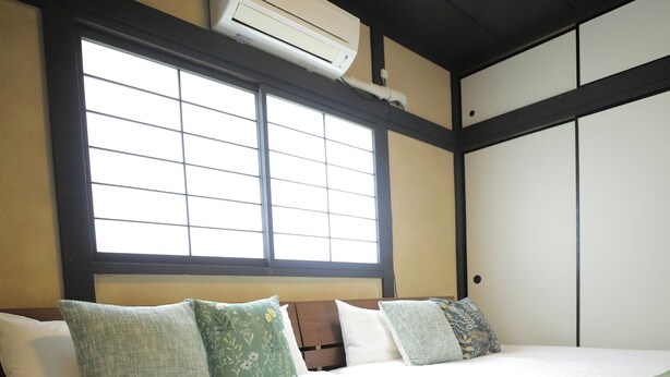 A hotel room with a bed, pillows, a window, and an air conditioning unit. - Neo Universal 01 (Osaka, Konohana, Nishikujo)