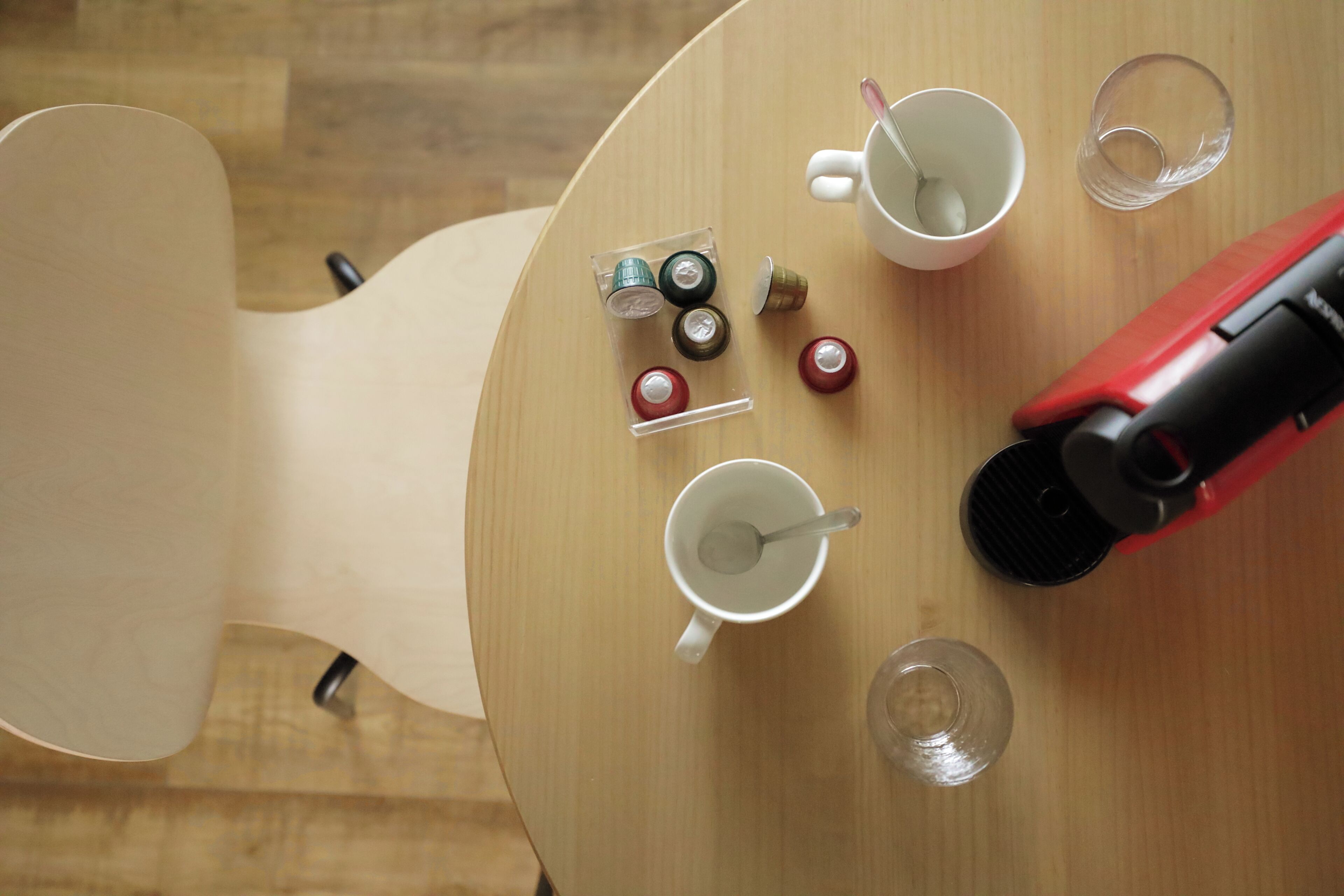 Une table ronde en bois, sur laquelle se trouvent une tasse blanche, un verre transparent, une bouilloire électrique rouge et plusieurs petites bouteilles.