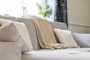 A sofa with a beige throw blanket and pillows, a lamp, and a plant in the background. - Cosy Bungalow | Sleeps 7 | Free Hot Tub and WiFi (Leigh)
