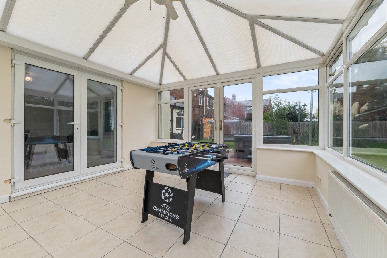 A sunroom with a foosball table, large windows, and a view of the backyard.