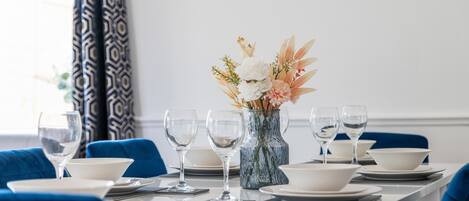 Une table de restaurant d’hôtel, mise avec des assiettes, des bols et des verres à vin, un vase rempli de fleurs et des chaises bleues.