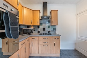 A compact kitchen with wooden cabinets, a microwave, and a gas stove. - Cosy Bungalow | Sleeps 7 | Free Hot Tub and WiFi (Leigh)
