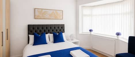 A bedroom with a bed, a nightstand, a chair, a window with blinds, and a painting on the wall.