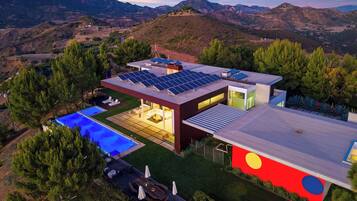 Uma casa moderna com piscina, painéis solares e vista para as colinas ao redor.