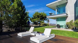 A modern outdoor seating area with lounge chairs and a dining table, overlooking a landscaped garden and a mountain view.