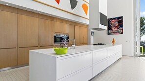 A modern kitchen with a large island, wooden cabinets, stainless steel appliances, and a flat-screen TV mounted on the wall. - The Malibu Art Estate by Avantstay Infinity Pool + Theater + Game Room 20 Private Acres (Malibu)