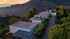 Un bâtiment moderne doté de panneaux solaires, entouré d’arbres et de montagnes.