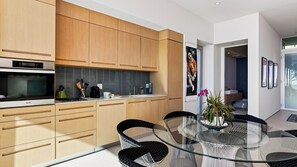 A modern kitchen with wooden cabinets, a built-in oven, and a glass dining table with chairs. - The Malibu Art Estate by Avantstay Infinity Pool + Theater + Game Room 20 Private Acres (Malibu)