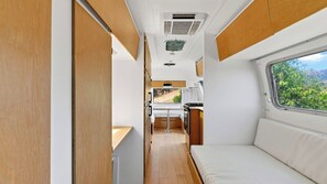 A compact RV interior with a kitchenette, a dining area, and a sleeping berth.