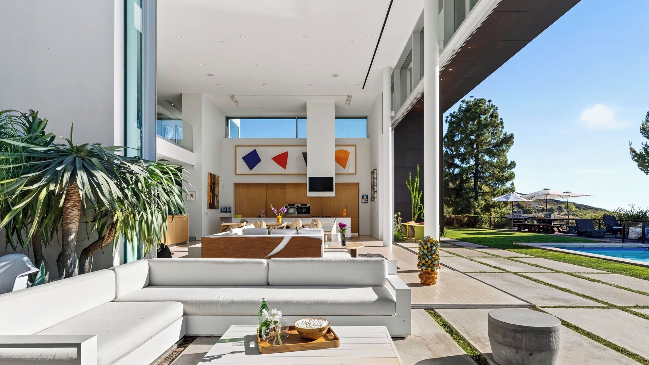 Uma sala de estar moderna com um sofá branco grande, uma área de jantar e vista para uma piscina.