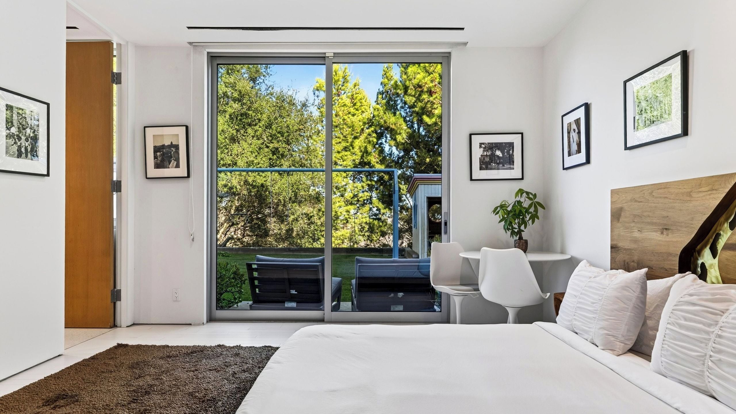 Quarto moderno com uma cama grande, uma escrivaninha e vista para um jardim por uma porta deslizante.