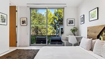 Quarto moderno com uma cama grande, uma escrivaninha e vista para um jardim por uma porta deslizante.