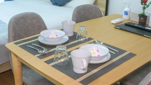 A neatly arranged hotel room with a bed, a dining table set with plates, cups, and cutlery, and a remote control on the table. - Best Friend (Fukuoka City Hakataku Katakasu)