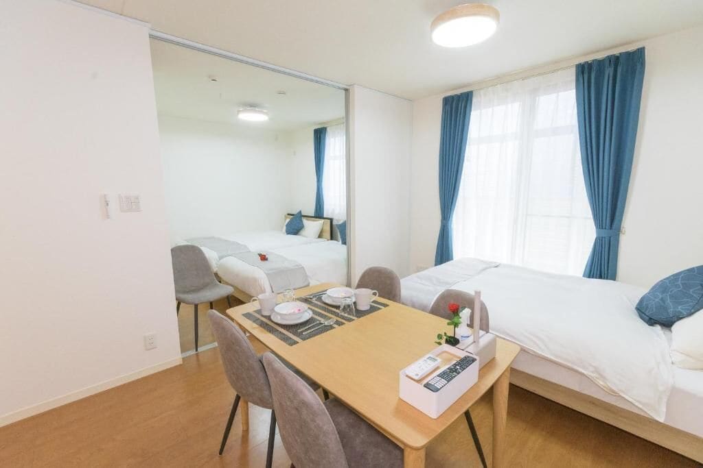 Habitación de hotel con cama, escritorio con silla, espejo y ventana con cortinas.