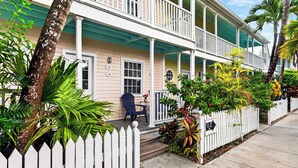 A two-story house with a porch, a chair, and a small table. - Salty Palm Retreat by Avantstay Shared Pool + Private Porch Steps to Beach + Old Town (Key West)