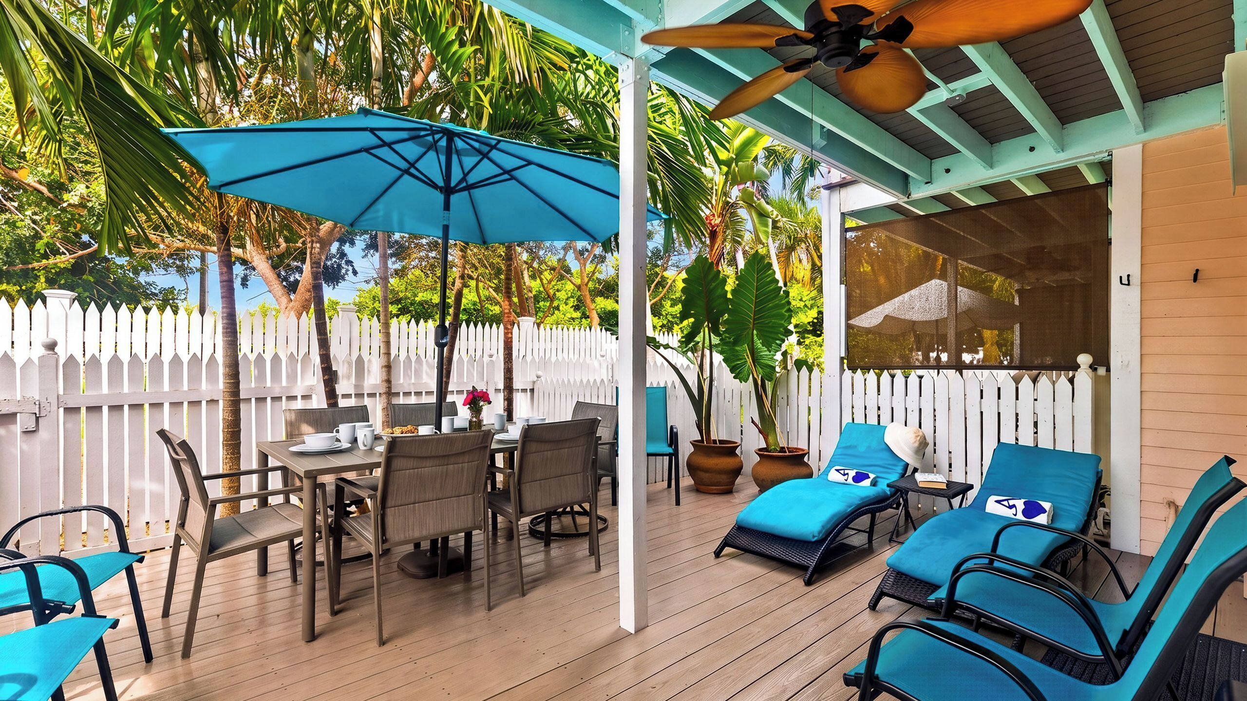 A covered outdoor patio with a table and chairs, lounge chairs, and umbrellas.