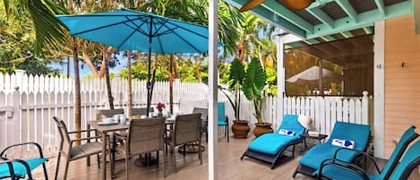 A covered outdoor patio with a table and chairs, lounge chairs, and umbrellas.