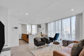 A modern living room with a sofa, armchairs, a coffee table, and a view of the city through large windows. - Gorgeous 3rd Floor 3 BRM Apartment (Broadbeach)