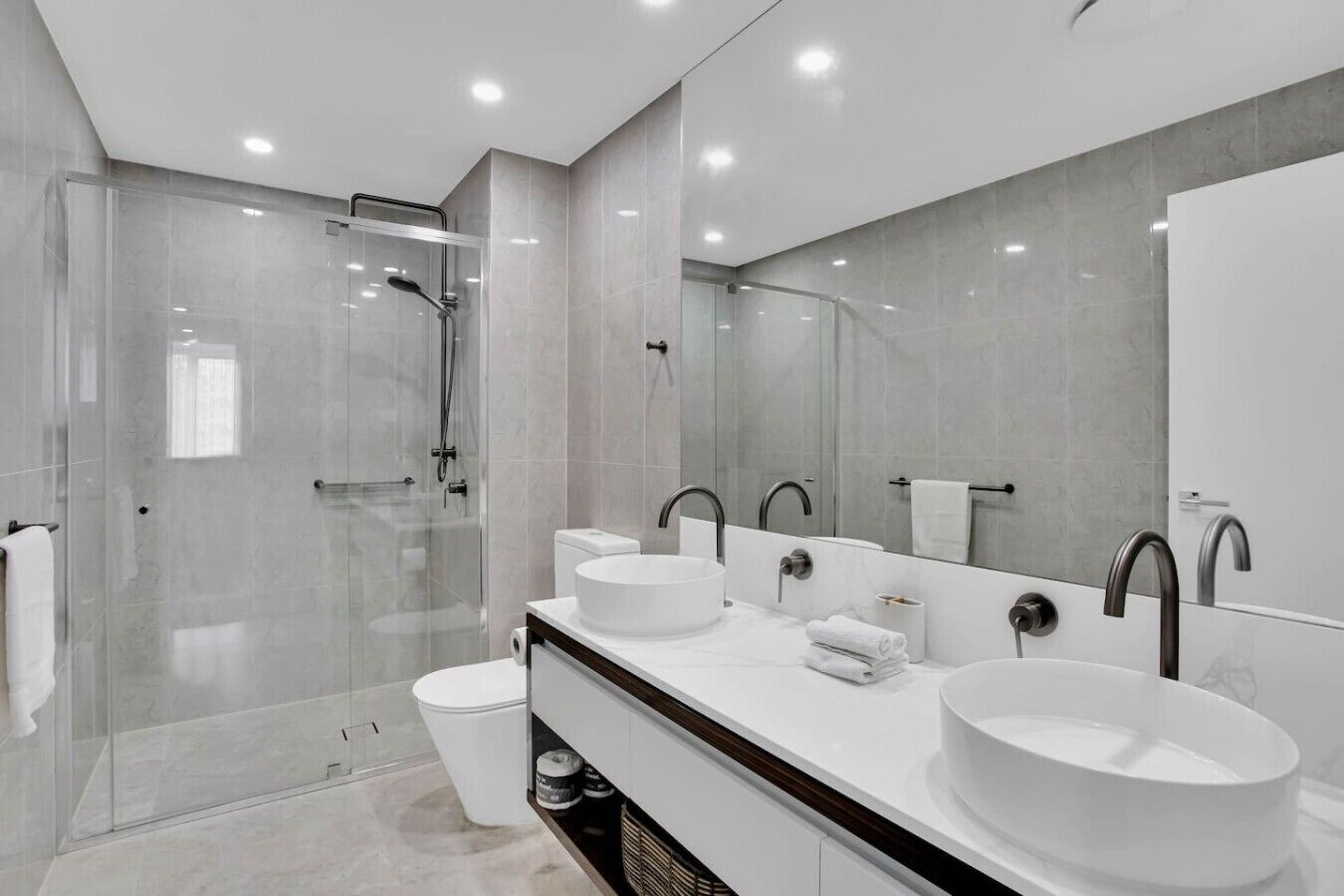 A modern bathroom with a glass-enclosed shower, two sinks, and a large mirror.