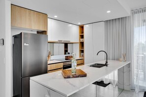 A modern kitchen with a built-in refrigerator, a marble countertop, and a sleek faucet. - Gorgeous 3rd Floor 3 BRM Apartment (Broadbeach)