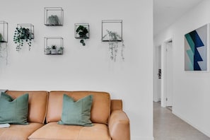 A modern interior with a leather sofa, green cushions, and wall-mounted planters with various plants. - Gorgeous 3rd Floor 3 BRM Apartment (Broadbeach)
