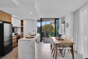 Eine moderne Küche mit integrierter Kochinsel, ein Essbereich mit Tisch und Stühlen sowie ein Balkon mit Stadtblick.