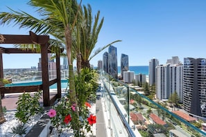 A balcony with a view of a city skyline, palm trees, and a pool. - Gorgeous 3rd Floor 3 BRM Apartment (Broadbeach)