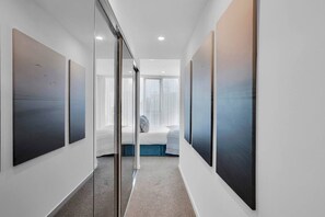 Ein modernes Hotelzimmer mit Glastrennwand, einem Bett mit blauer Kopfteil und Kunstwerken an den Wänden.