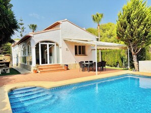 Ett hus med en swimmingpool, utemöbler och en täckt uteplats.