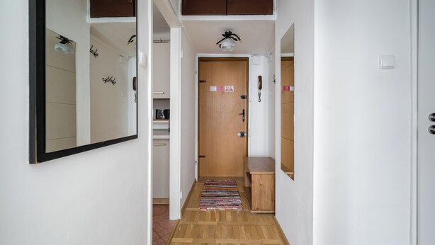 A narrow hallway with a wooden floor, a door with a telephone, and a mirror on the wall. - Żelazna Classy Nest Apartment (Warszawa)