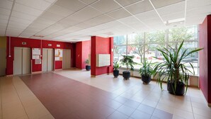 A spacious lobby with a high ceiling, red walls, and a tiled floor. There are several potted plants and a large window providing a view of the outside. - Żelazna Classy Nest Apartment (Warszawa)