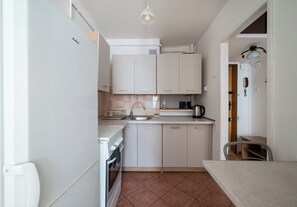 Uma cozinha compacta com armários brancos, pia, fogão e chaleira.