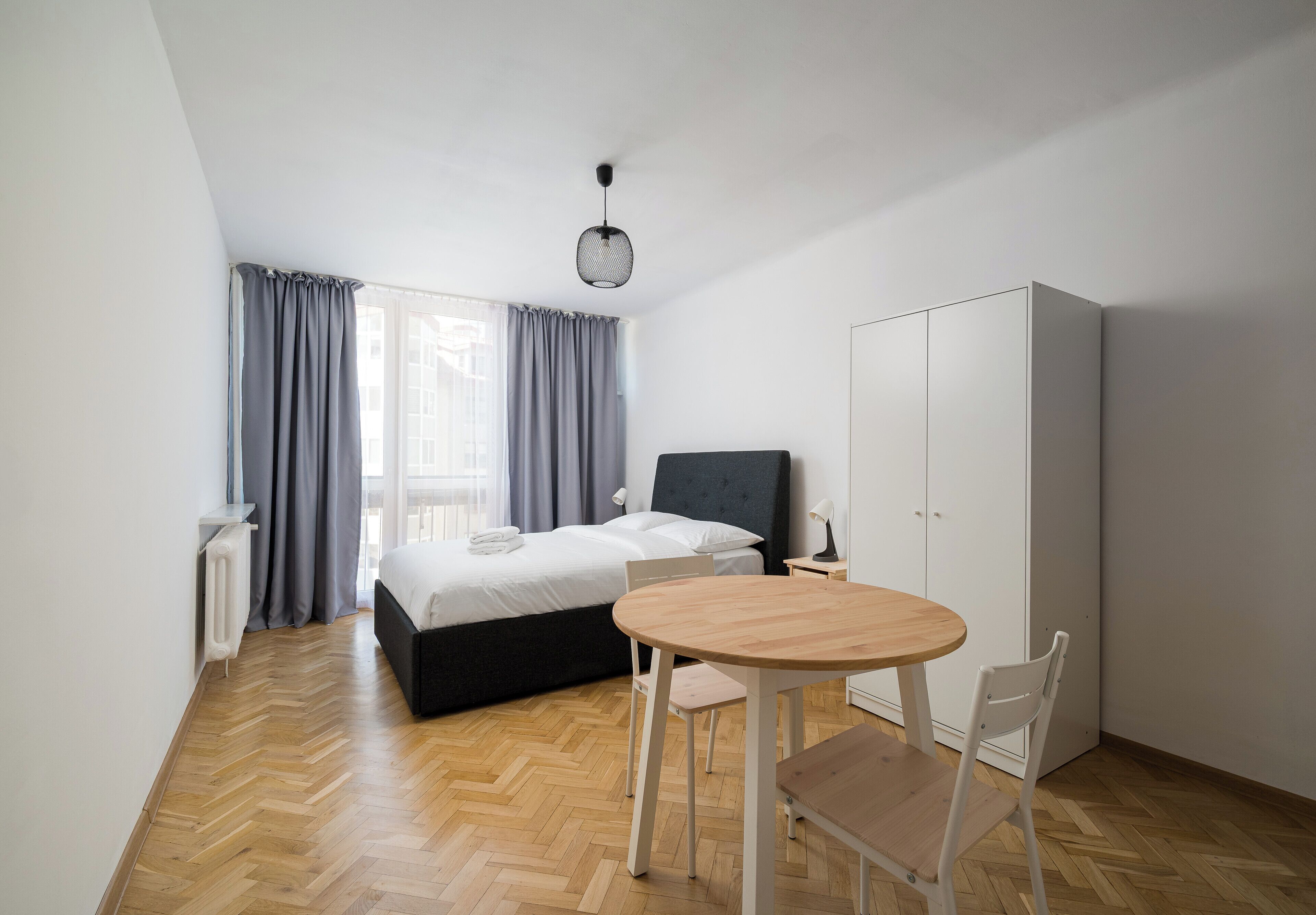 A bedroom with a bed, a desk, a chair, a wardrobe, and a round table.