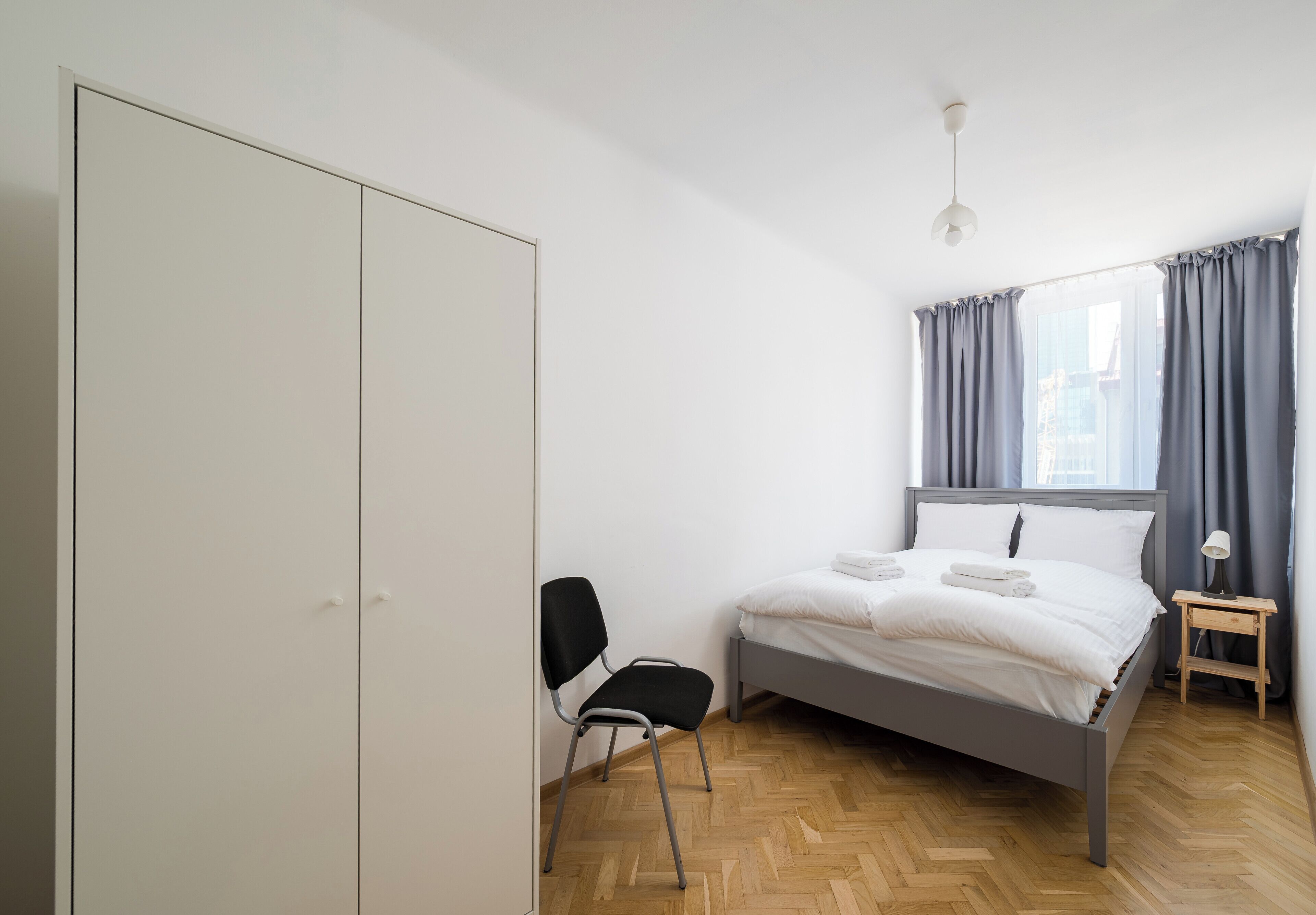 Une chambre à coucher avec un lit, une chaise, une table de chevet et une fenêtre avec des rideaux.