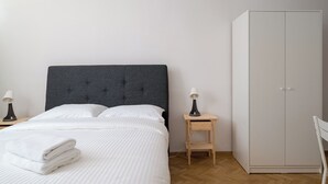 A bedroom with a bed, a bedside table with a lamp, a wardrobe, and a chair. - Żelazna Classy Nest Apartment (Warszawa)