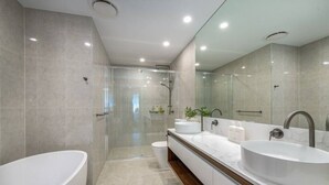 Une salle de bain moderne dotée d’une grande baignoire sur pieds, d’une douche à l’italienne et d’un long meuble-lavabo avec deux vasques.