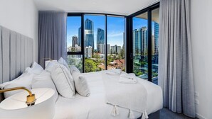 Une chambre d’hôtel moderne avec un lit aux lignes courbes, de grandes fenêtres et une vue sur la ville.