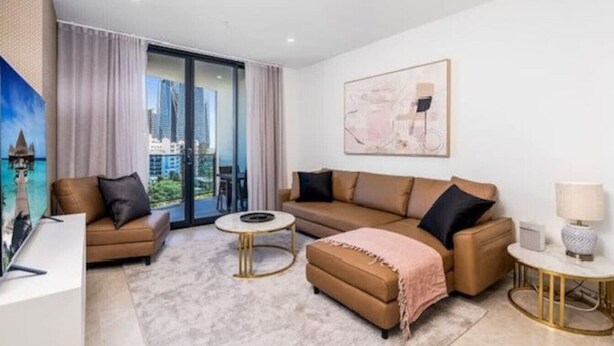 Un salon moderne avec un canapé, un pouf, une table basse et un tableau accroché au mur.