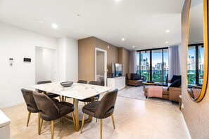 Eine moderne Wohnung mit Essbereich, einem Wohnzimmer inklusive Sofa und Fernseher sowie einem Balkon mit Blick auf die Stadt.