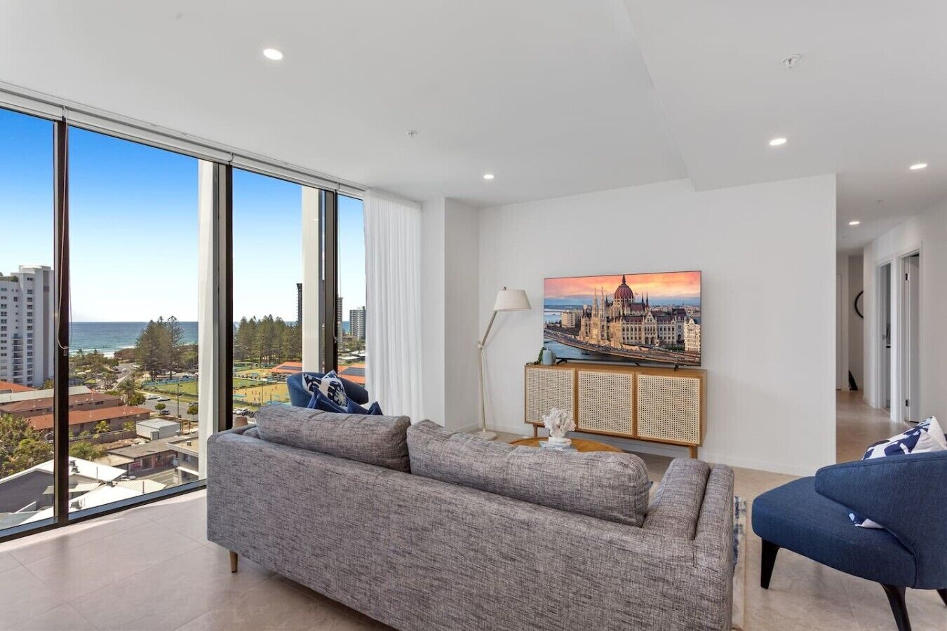 Een moderne woonkamer met een groot raam, een bank, een stoel en een schilderij van een stadsgezicht.