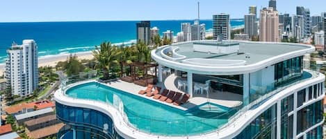 Ein modernes Hotel mit einem Dachpool im Infinity-Stil, das Blick auf den Ozean und die Stadtkulisse bietet.