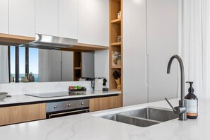 A modern kitchen with a built-in stove, a stainless steel sink, and a wooden cabinet. - Luxury 3 Brm Apt with Beach Views Lv9 (Broadbeach)