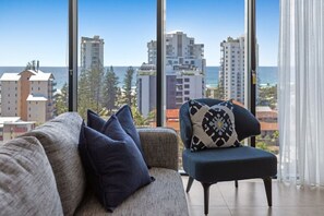 Ein modernes Wohnzimmer mit Sofa und Sesseln, große Fenster mit Blick auf die Stadt und das Meer.