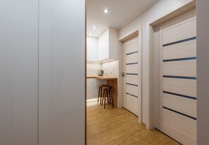 Un couloir étroit doté d’un plancher en bois, de murs blancs et d’un coin cuisine avec un comptoir et des tabourets.