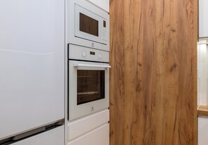 A kitchen with a built-in microwave and oven, a wooden panel, and a white cabinet. - Pole Mokotowskie Modern Nest Apartment (Warszawa)