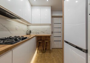 Une cuisine moderne avec des meubles blancs, un plan de travail en bois, une cuisinière à gaz et deux tabourets en bois.
