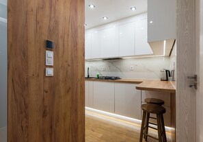 A modern kitchen with white cabinets, a wooden countertop, a gas stove, and a wooden stool. - Pole Mokotowskie Modern Nest Apartment (Warszawa)