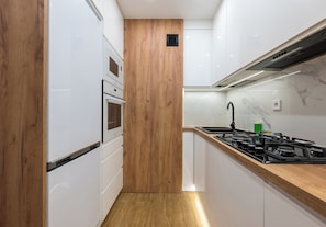 A modern kitchen with white cabinetry, a wooden accent wall, a gas stove, and a built-in oven. - Pole Mokotowskie Modern Nest Apartment (Warszawa)